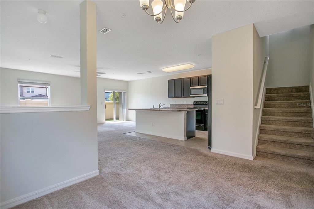An open-concept living area features a kitchen with dark cabinets, an island, and carpeted stairs — 3521 SENECA CLUB LOOP UNIT 103C, ORLANDO, FL