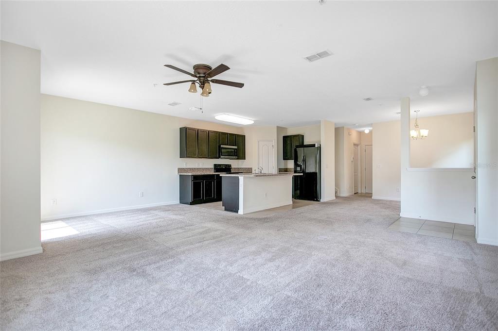 An open-concept living area features gray carpeting, a kitchen with dark cabinets, and an island — 3521 SENECA CLUB LOOP UNIT 103C, ORLANDO, FL