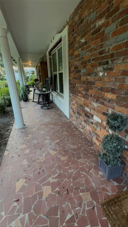 A covered brick porch features a flagstone floor, white columns, and a rocking chair — 719 AVENUE Q SE, WINTER HAVEN, FL