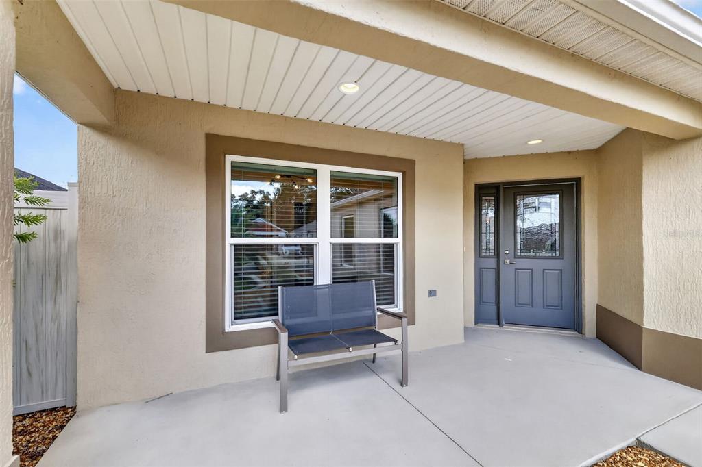 A covered front porch features a gray bench, a window, and a dark gray front door — 4686 HILES PLACE, THE VILLAGES, FL