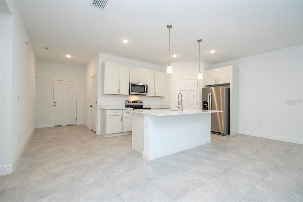 A modern kitchen features white cabinets, stainless steel appliances, a center island, and tile flooring — 8 LOCUST RUN PASS, OCALA, FL