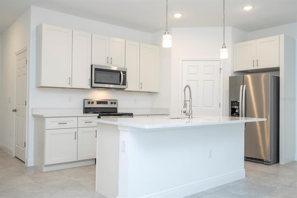 A kitchen features white cabinets, stainless steel appliances, a center island, and light-colored countertops — 8 LOCUST RUN PASS, OCALA, FL