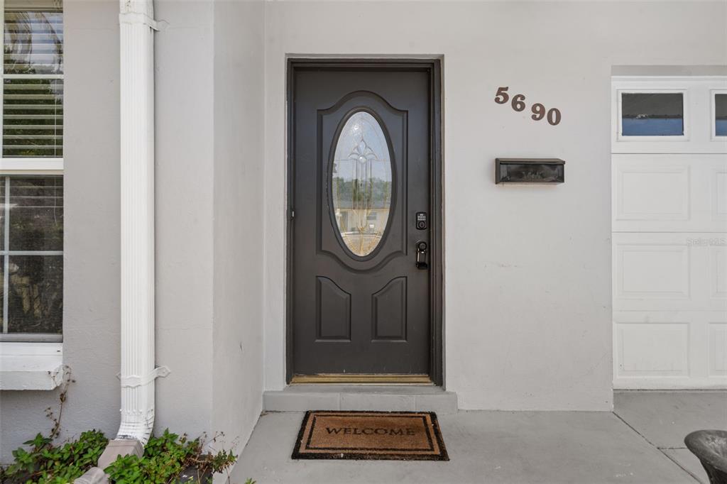 A dark front door with an oval glass insert sits beside a white garage door — 5690 6TH STREET S, ST PETERSBURG, FL