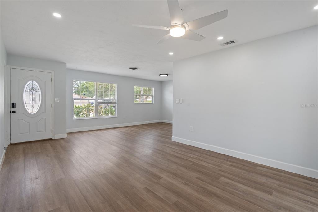 A bright living room features light wood-look flooring, white walls, and a ceiling fan — 5690 6TH STREET S, ST PETERSBURG, FL