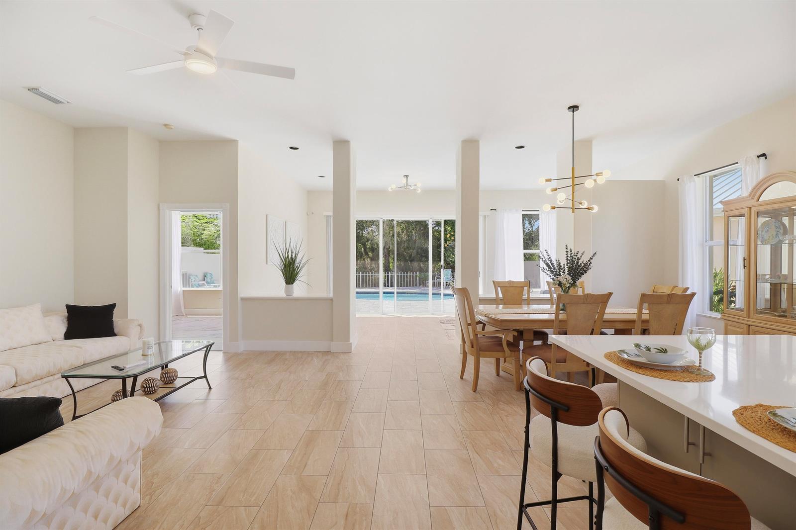 An open-concept living and dining area features tile flooring, a pool view, and neutral decor — 7756 SE Bay Cedar Circle, Hobe Sound FL 33455, HOBE SOUND, FL