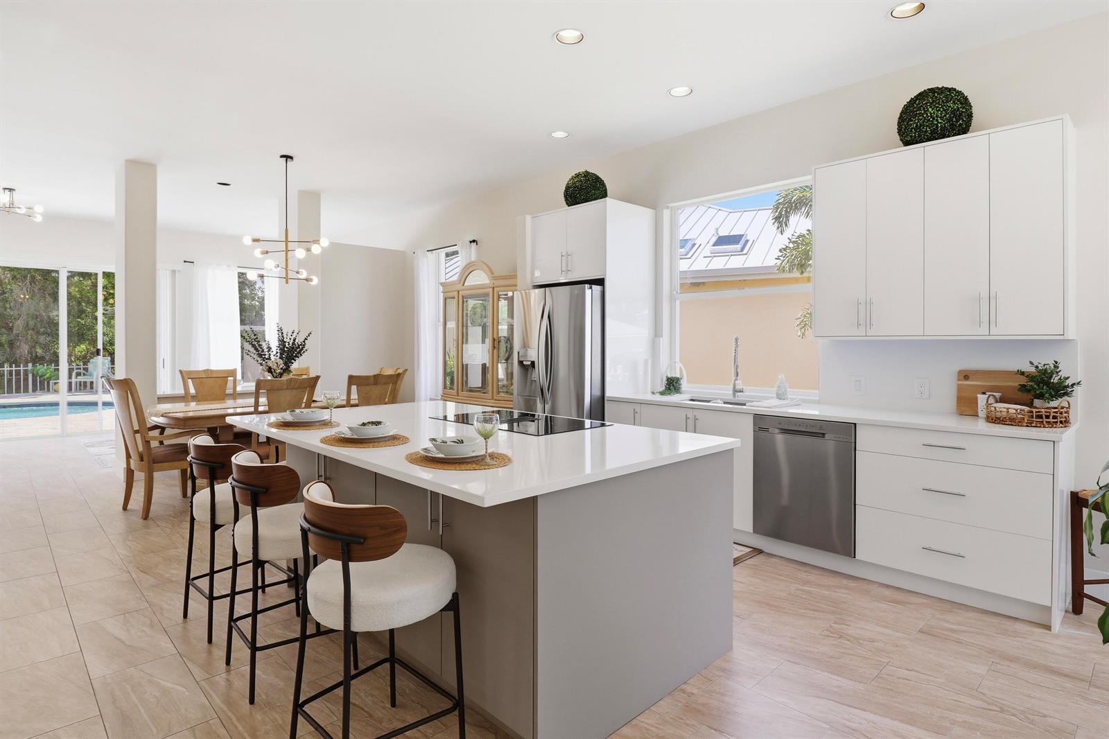 A modern kitchen features a large gray island, white cabinetry, and an adjacent dining area — 7756 SE Bay Cedar Circle, Hobe Sound FL 33455, HOBE SOUND, FL