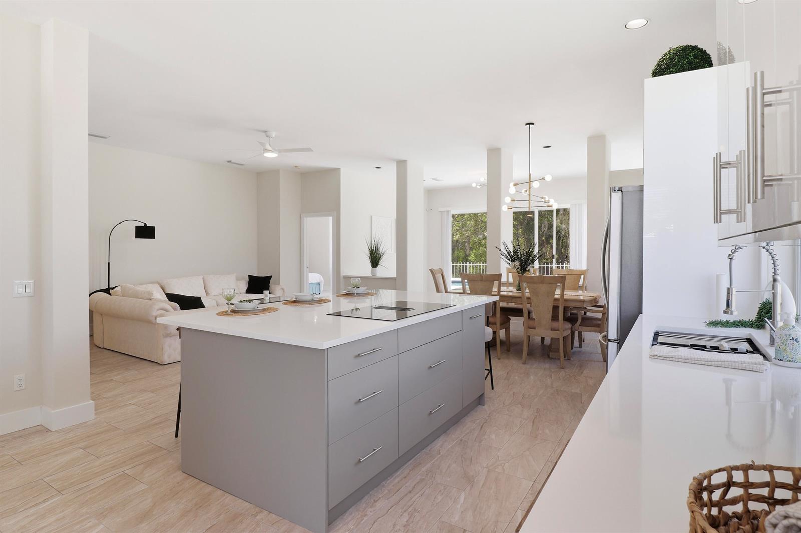 A modern open-concept kitchen with a gray island, white countertops, and adjacent living and dining areas — 7756 SE Bay Cedar Circle, Hobe Sound FL 33455, HOBE SOUND, FL