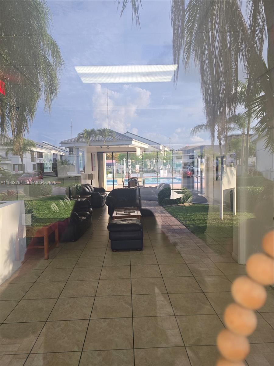 A view through a glass door shows a tiled lobby with leather furniture and pool access — 252 NE 212th Ter, Miami FL 33179, MIAMI, FL