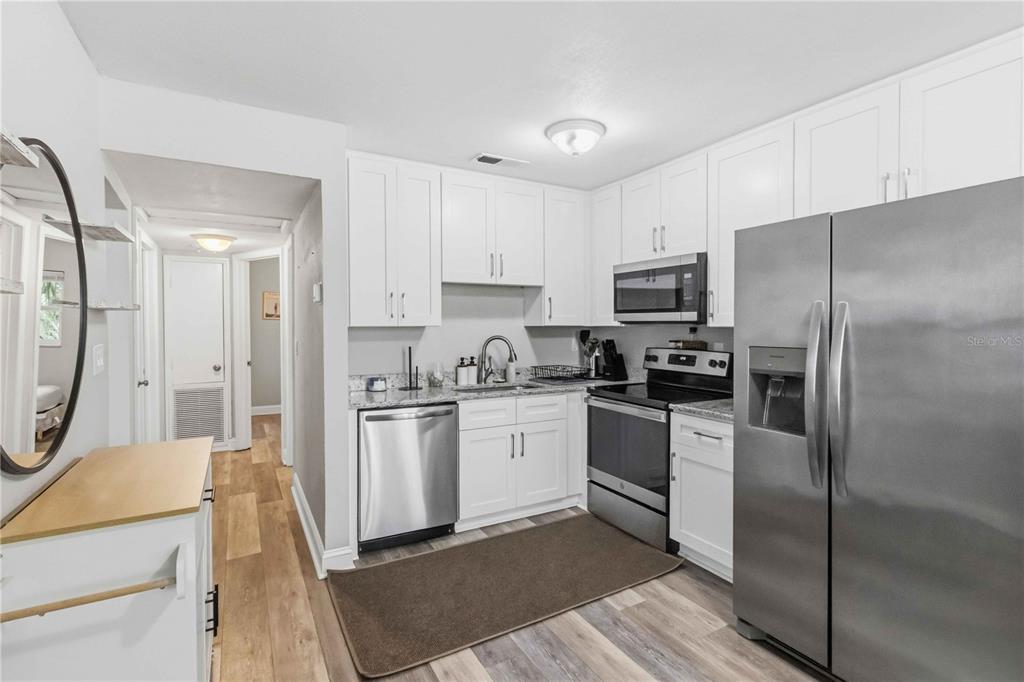 A kitchen features white cabinets, stainless steel appliances, granite countertops, and light wood-look flooring — 7012 40TH AVENUE N, ST PETERSBURG, FL