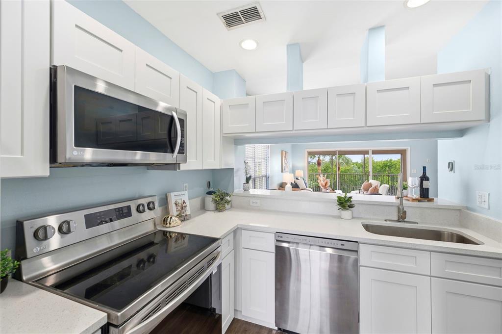 A kitchen with white cabinets, stainless steel appliances, and a pass-through window to the living area — 11541 SHIPWATCH DRIVE UNIT 1011, LARGO, FL