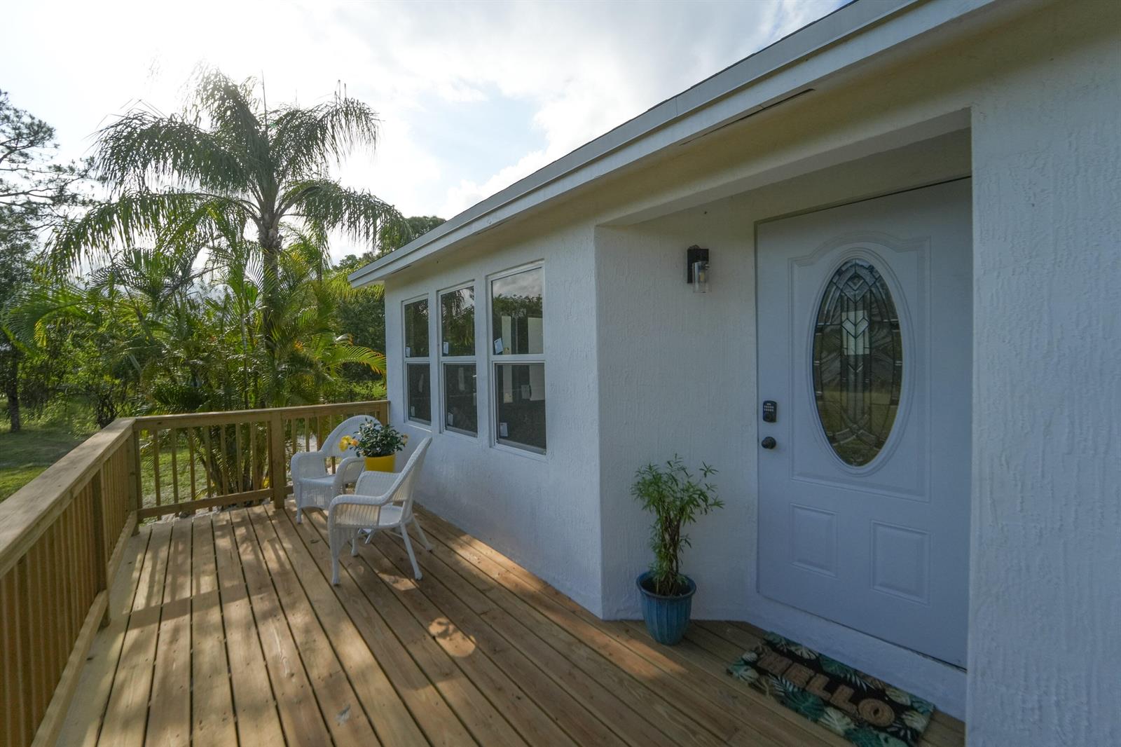 A white house exterior features a wooden deck with two chairs and a front door — 13555 150th Court N, Jupiter FL 33478, JUPITER, FL
