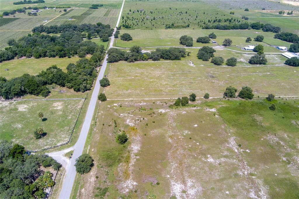 An aerial view shows a rural landscape with a paved road, open fields, and trees — WHITE CLAY PIT ROAD, HAINES CITY, FL