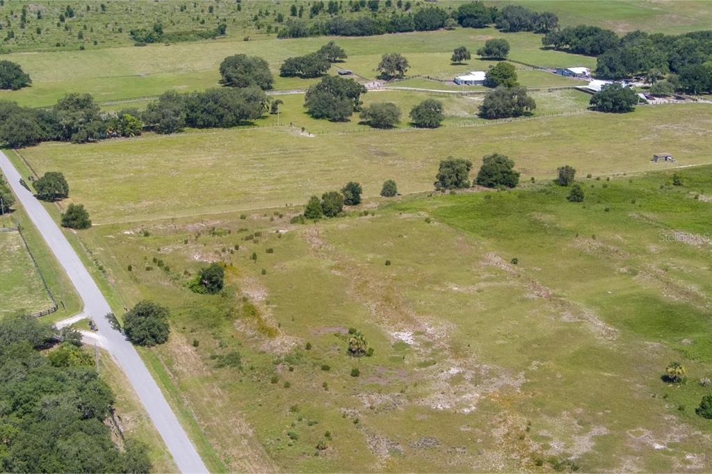 An aerial view shows a large, grassy rural property with scattered trees and a paved road — WHITE CLAY PIT ROAD, HAINES CITY, FL