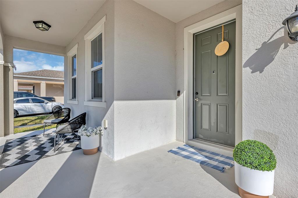 A covered front porch features a gray door, two chairs on a rug, and potted plants — 3471 DOVETAIL AVENUE, KISSIMMEE, FL
