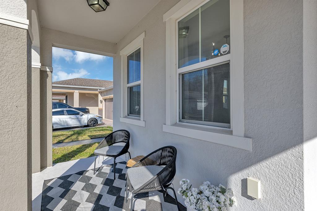 A covered front porch features two black chairs, a patterned rug, and two windows — 3471 DOVETAIL AVENUE, KISSIMMEE, FL