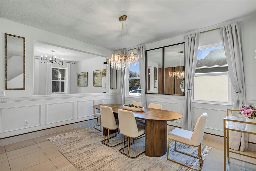 A dining room features an oval wooden table, cream chairs, a crystal chandelier, and wall mirrors — 3471 DOVETAIL AVENUE, KISSIMMEE, FL