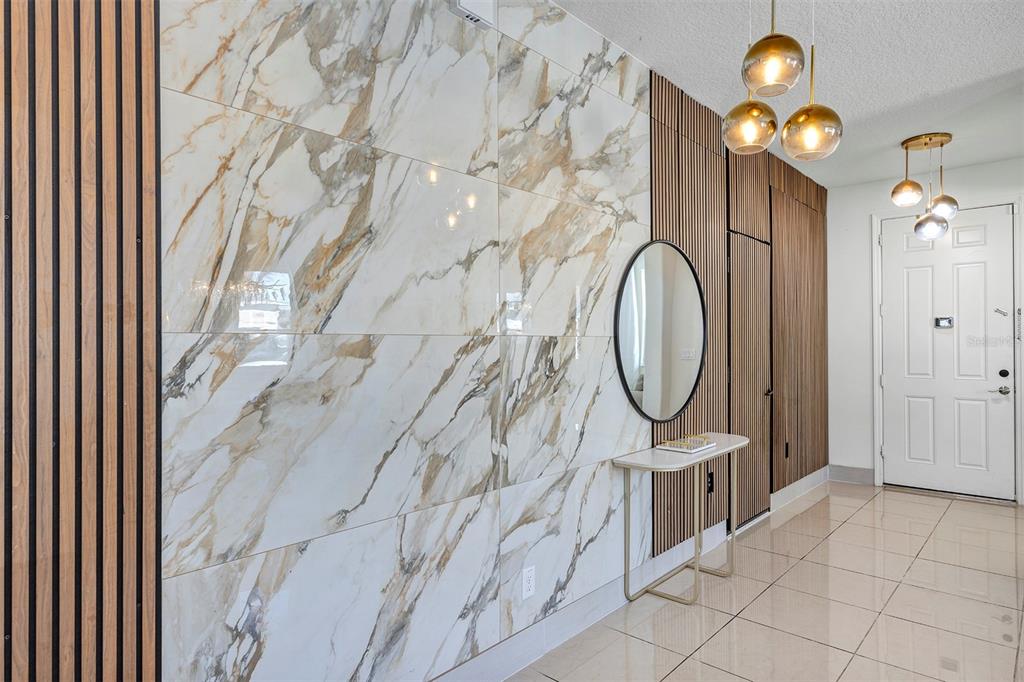 An entryway features a large marble-tiled accent wall, vertical wood slats, and a modern console table — 3471 DOVETAIL AVENUE, KISSIMMEE, FL