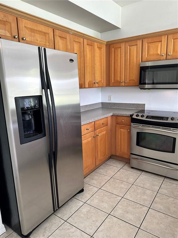 A kitchen featuring wood cabinets, stainless steel appliances, and light-colored tile flooring — 8961 IRON OAK AVENUE, TAMPA, FL