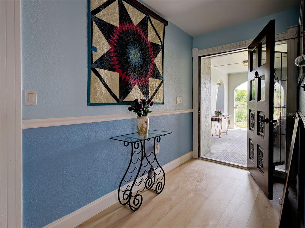 An entryway features light blue walls, a star-patterned wall hanging, a glass console table, and flooring — 107 PECKHAM STREET SW, PORT CHARLOTTE, FL