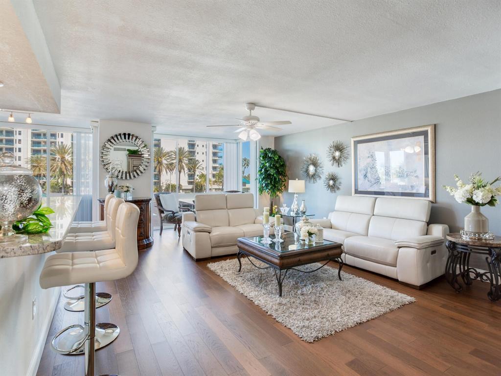 A living room features white leather sofas, a glass-topped coffee table, and hardwood flooring — 660 ISLAND WAY UNIT 202, CLEARWATER BEACH, FL