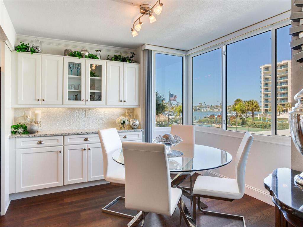 A dining area features white cabinets, a glass table, and large windows overlooking a marina — 660 ISLAND WAY UNIT 202, CLEARWATER BEACH, FL