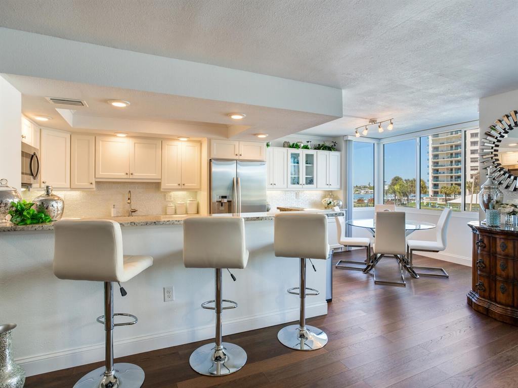 A kitchen with white cabinets, granite countertops, and bar seating overlooks a dining area — 660 ISLAND WAY UNIT 202, CLEARWATER BEACH, FL