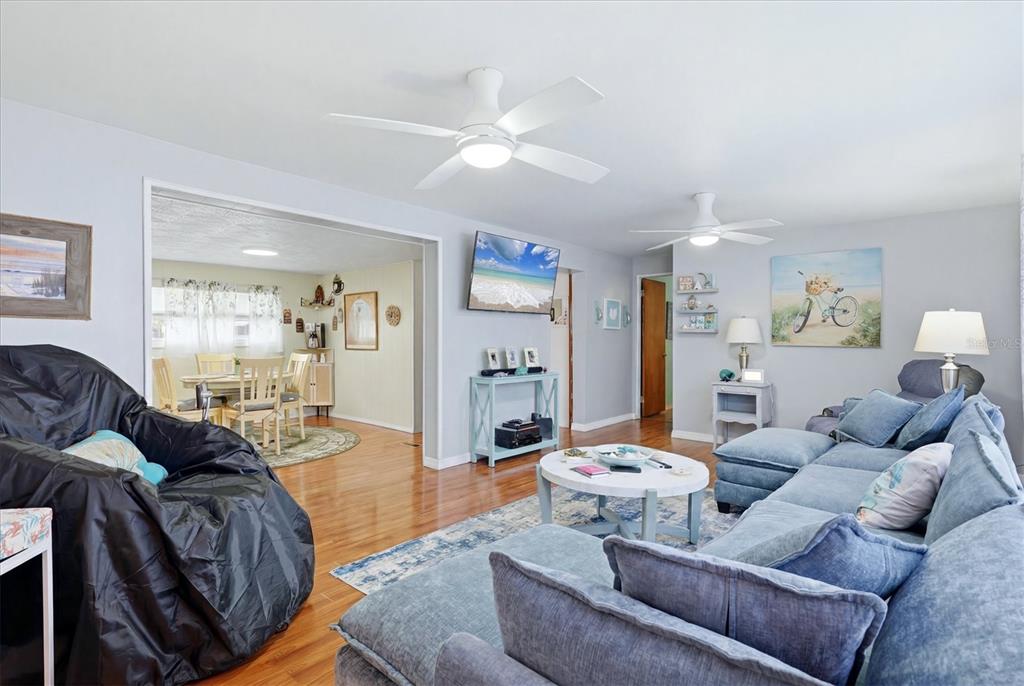 A living room with a blue sectional sofa, hardwood floors, and a dining area beyond — 1006 42ND AVENUE DRIVE E, ELLENTON, FL