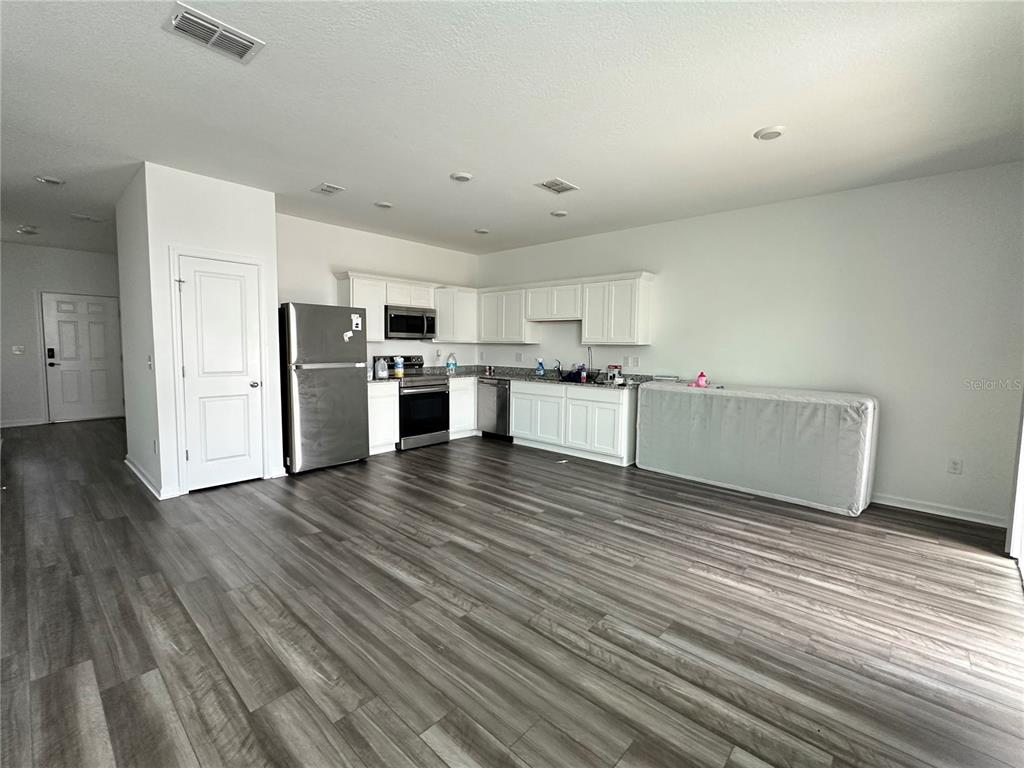 An open-concept kitchen features white cabinets, stainless steel appliances, and wood-look flooring — 6287 BUCKET COURT, GIBSONTON, FL