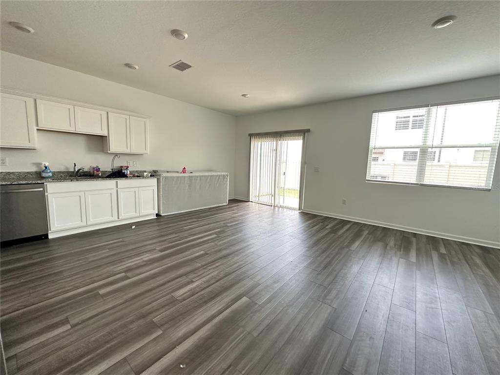 An open-concept kitchen and living area features white cabinets, granite countertops, and wood-look flooring — 6287 BUCKET COURT, GIBSONTON, FL