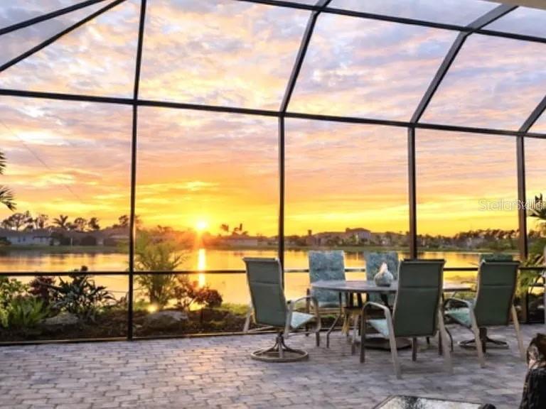 A screened-in patio with outdoor furniture overlooks a lake during a sunset — 11516 RENAISSANCE BOULEVARD, VENICE, FL