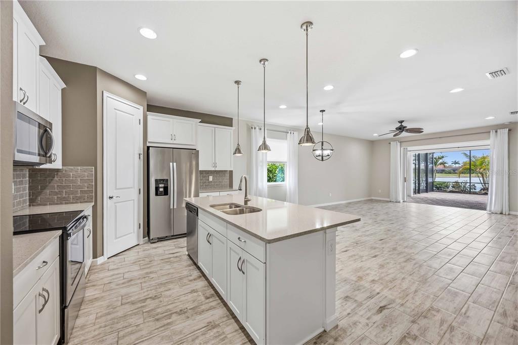 A kitchen with white cabinets, stainless steel appliances, and an island opens to a living area — 11516 RENAISSANCE BOULEVARD, VENICE, FL