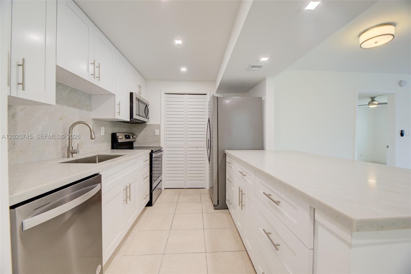 A modern kitchen features white cabinetry, stainless steel appliances, and light-colored countertops and flooring — 200 LAKEVIEW DR # 211, Weston FL 33326, WESTON, FL