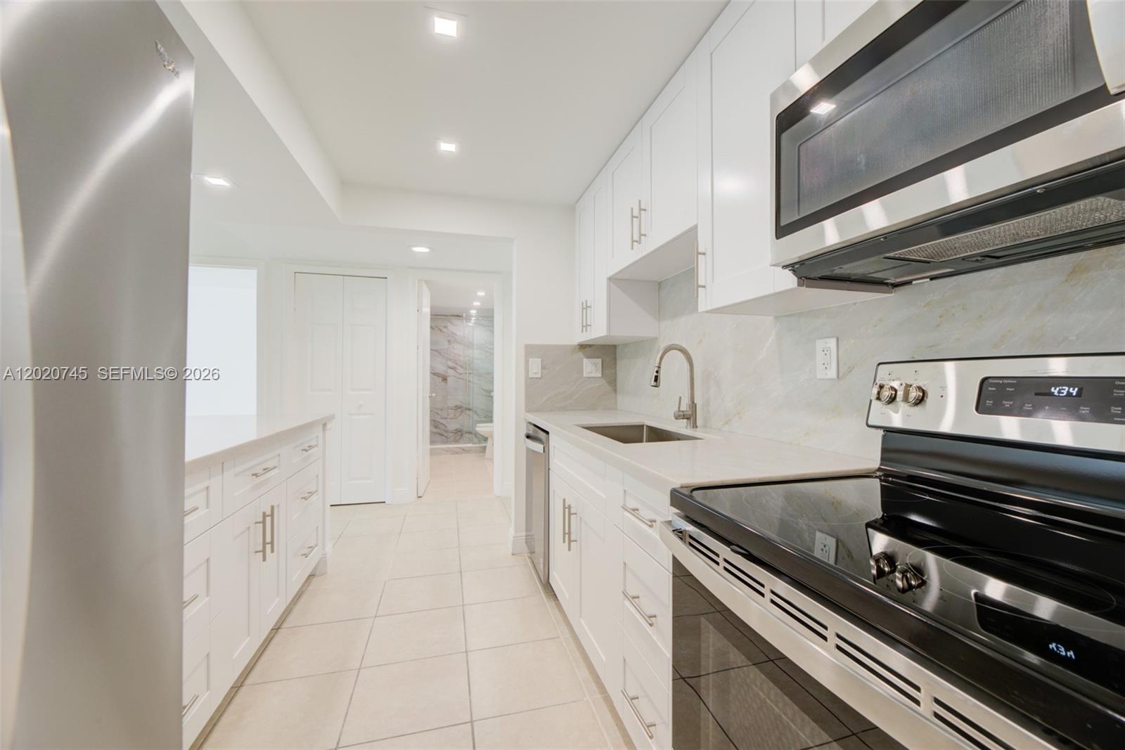A modern galley kitchen features white cabinets, stainless steel appliances, and light-colored stone countertops — 200 LAKEVIEW DR # 211, Weston FL 33326, WESTON, FL