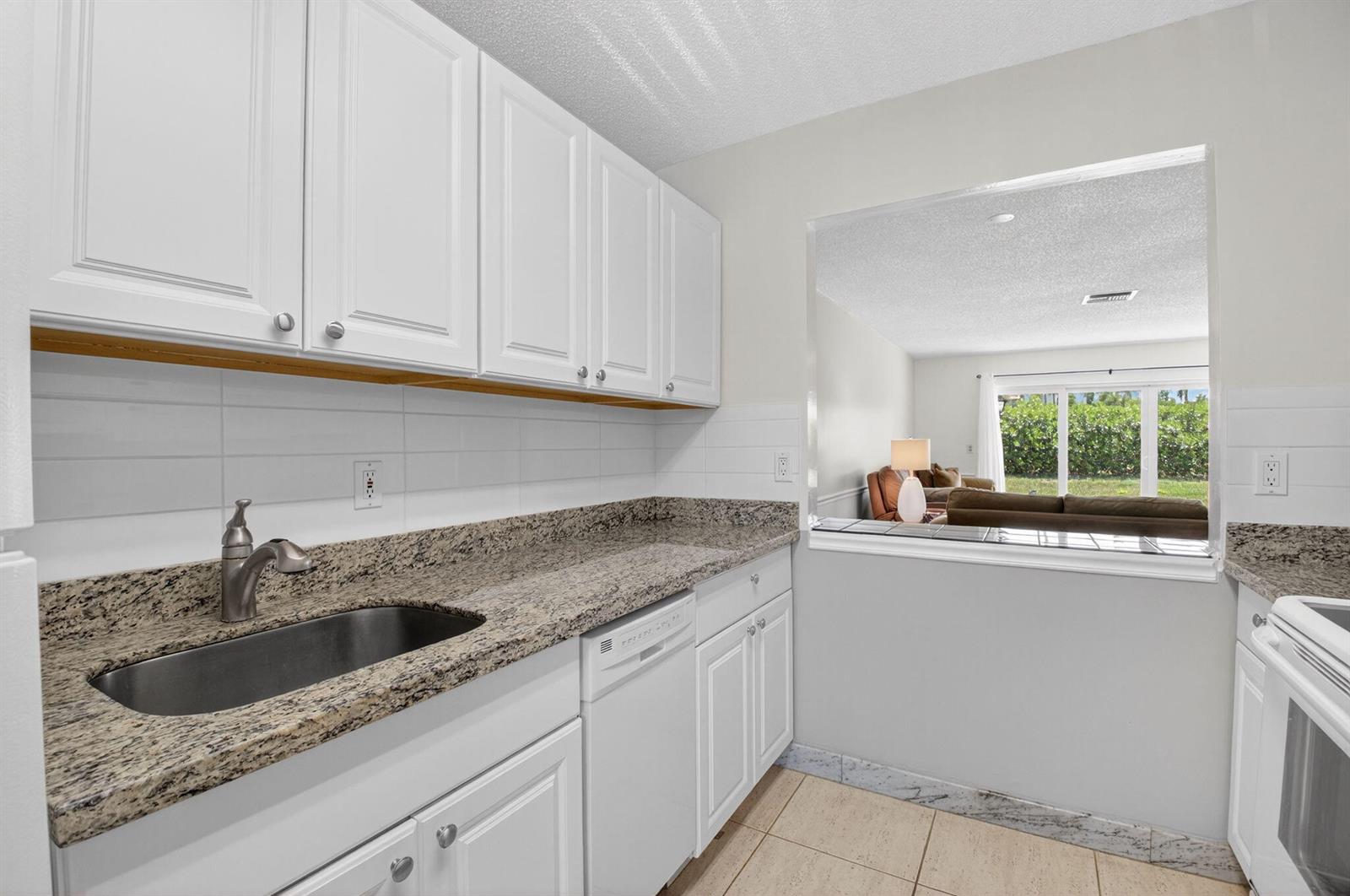 A kitchen features white cabinets, granite countertops, a stainless steel sink, and a pass-through window — 13984 Vía Flora # B, Delray Beach FL 33484, DELRAY BEACH, FL
