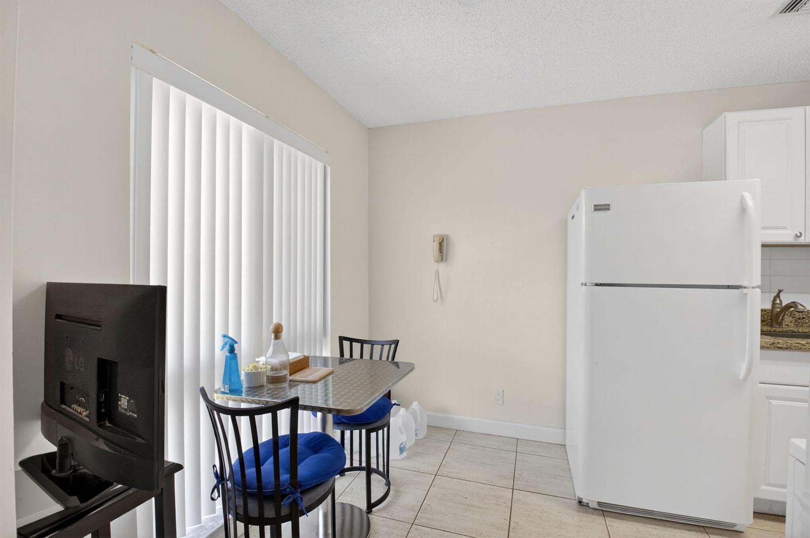 A small dining area features a table with two chairs, a white refrigerator, and tile flooring — 13984 Vía Flora # B, Delray Beach FL 33484, DELRAY BEACH, FL