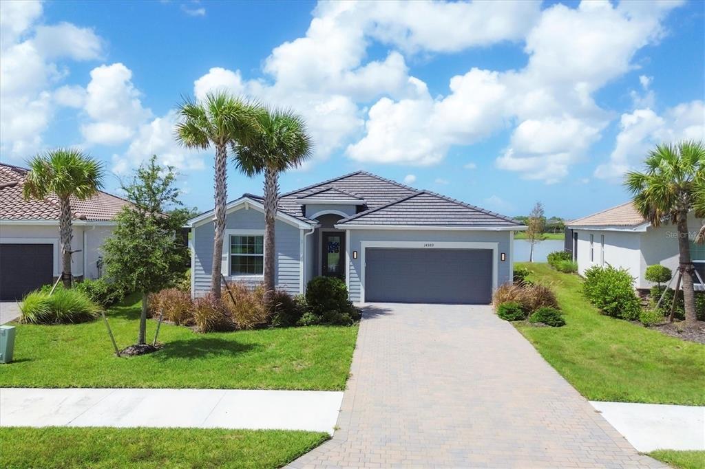 A single-story house with a gray exterior, tiled roof, and a paved driveway faces a lake — 14589 PONCE DE LEON TRAIL, PORT CHARLOTTE, FL