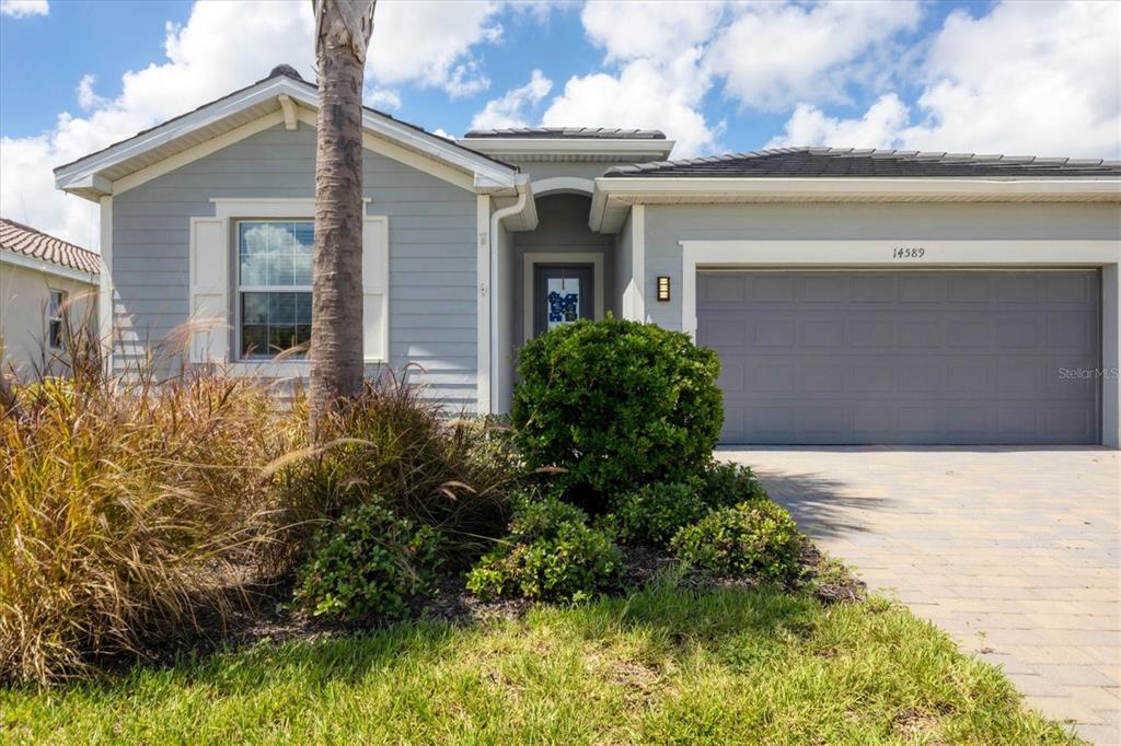 A single-story house with light blue siding, a gray garage door, and a landscaped front yard — 14589 PONCE DE LEON TRAIL, PORT CHARLOTTE, FL