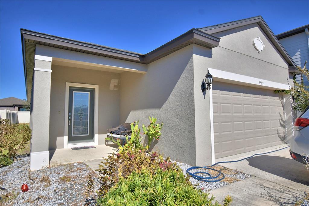 The exterior of a single-story house features a gray garage door and a covered entryway — 3589 ROCK CREEK LANE, KISSIMMEE, FL