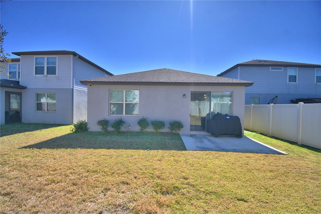 The exterior rear view of a house shows a small concrete patio and lawn — 3589 ROCK CREEK LANE, KISSIMMEE, FL