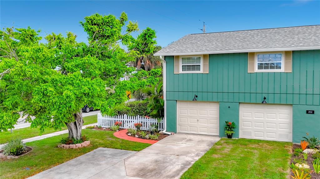 A two-story teal house features two garage doors and a large tree in the yard — 202 PEACOCK LANE UNIT A, HOLMES BEACH, FL