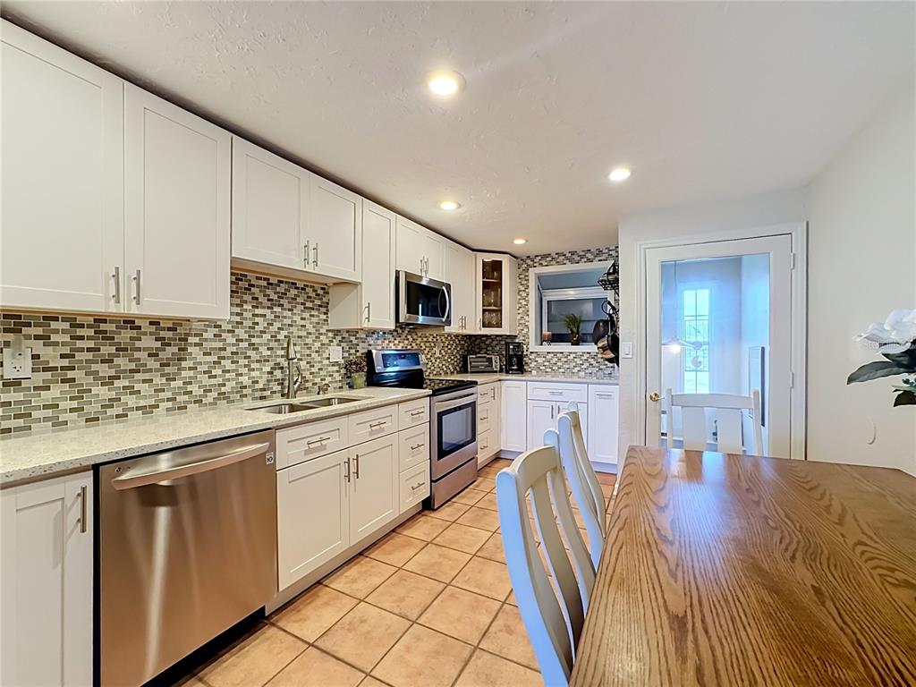 A kitchen features white cabinetry, stainless steel appliances, a mosaic tile backsplash, and tile flooring — 202 PEACOCK LANE UNIT A, HOLMES BEACH, FL