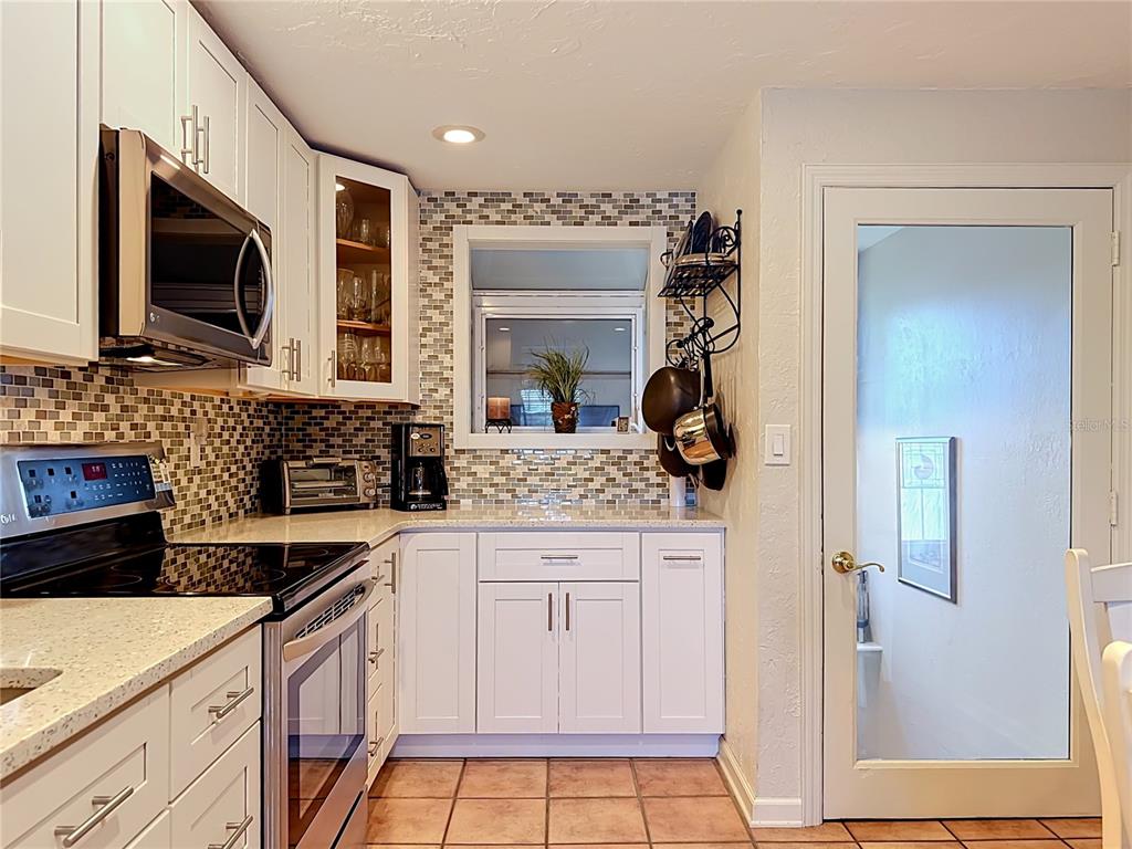 A kitchen features white cabinets, a mosaic tile backsplash, stainless steel appliances, and tile flooring — 202 PEACOCK LANE UNIT A, HOLMES BEACH, FL
