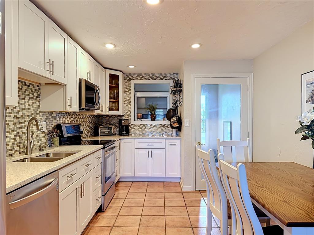 A kitchen features white cabinetry, a tiled backsplash, stainless steel appliances, and a dining table — 202 PEACOCK LANE UNIT A, HOLMES BEACH, FL