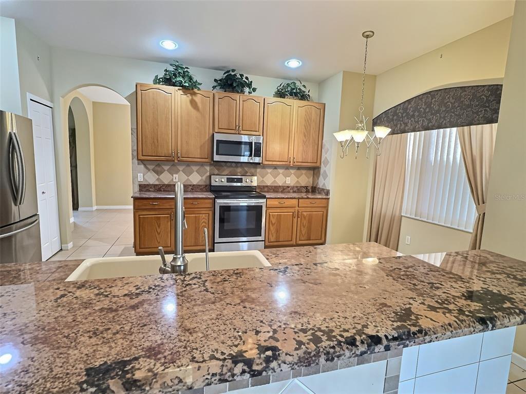 A kitchen features wood cabinets, granite countertops, stainless steel appliances, and a breakfast bar — 2414 HURON CIRCLE, KISSIMMEE, FL