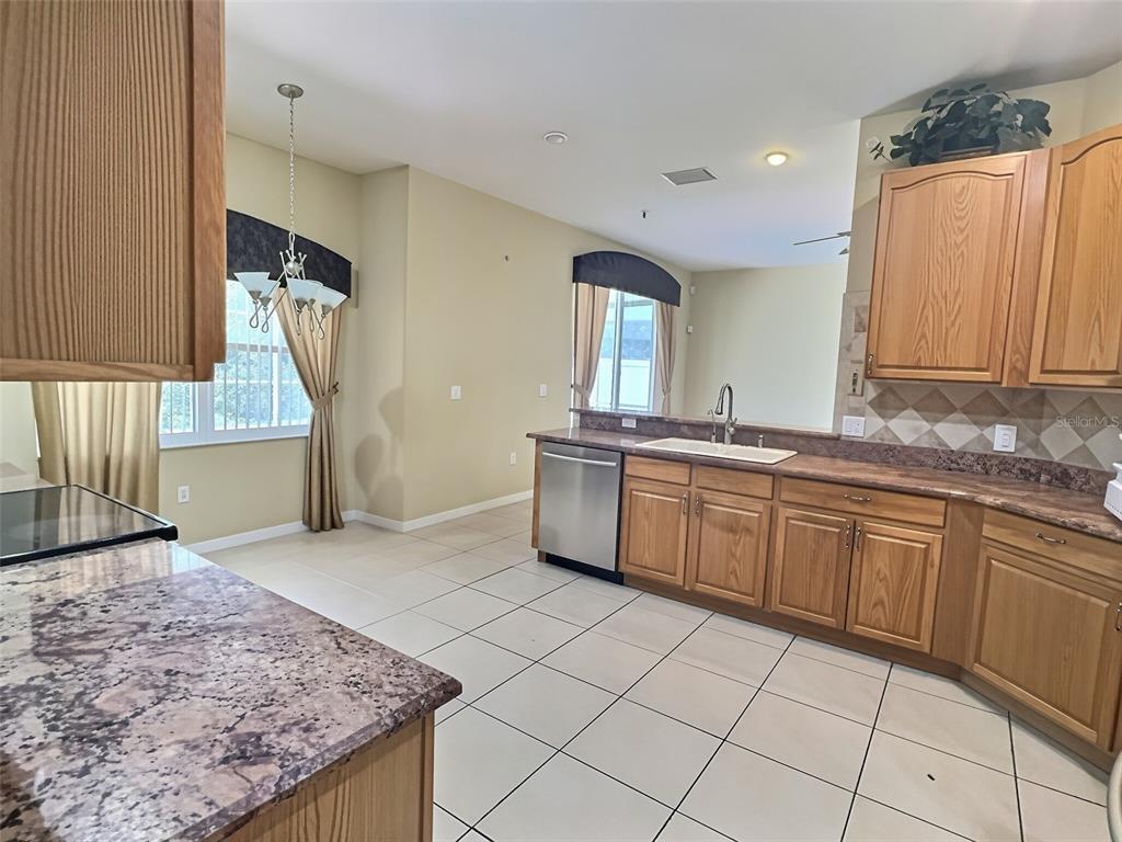 A kitchen features wood cabinets, granite countertops, stainless steel appliances, and light-colored floor tiles — 2414 HURON CIRCLE, KISSIMMEE, FL