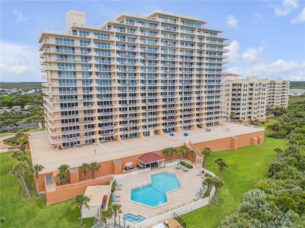 An aerial view of a tall beachfront condominium building with a pool and hot tub — 257 MINORCA BEACH WAY UNIT 406, NEW SMYRNA BEACH, FL