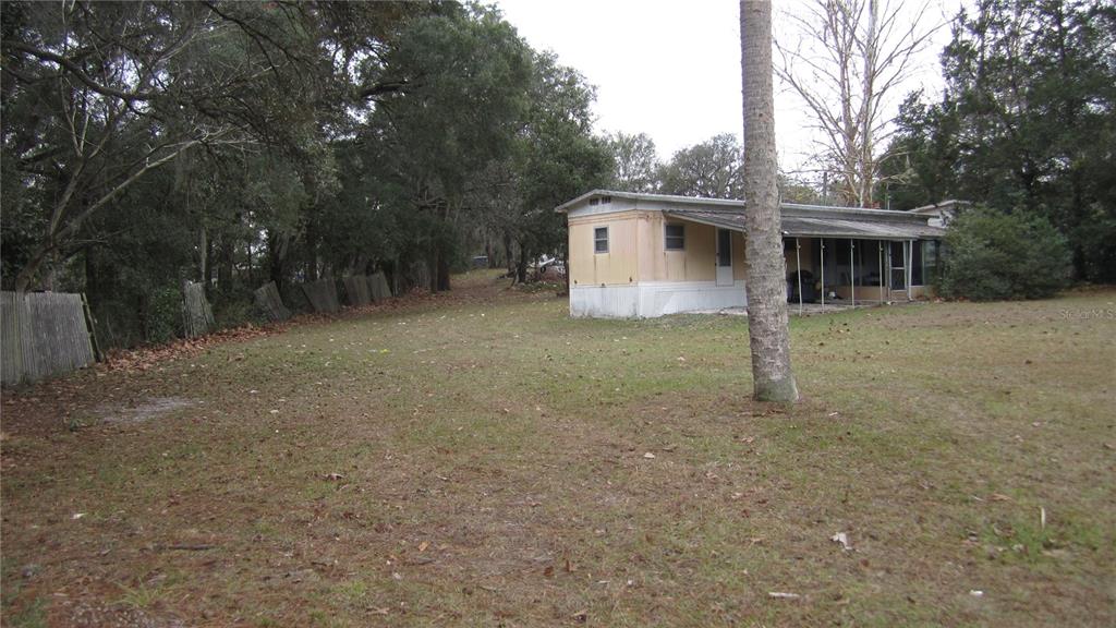 A single-story mobile home sits on a grassy lot surrounded by trees and a fence — 6973 N CARL G ROSE HWY, HERNANDO, FL