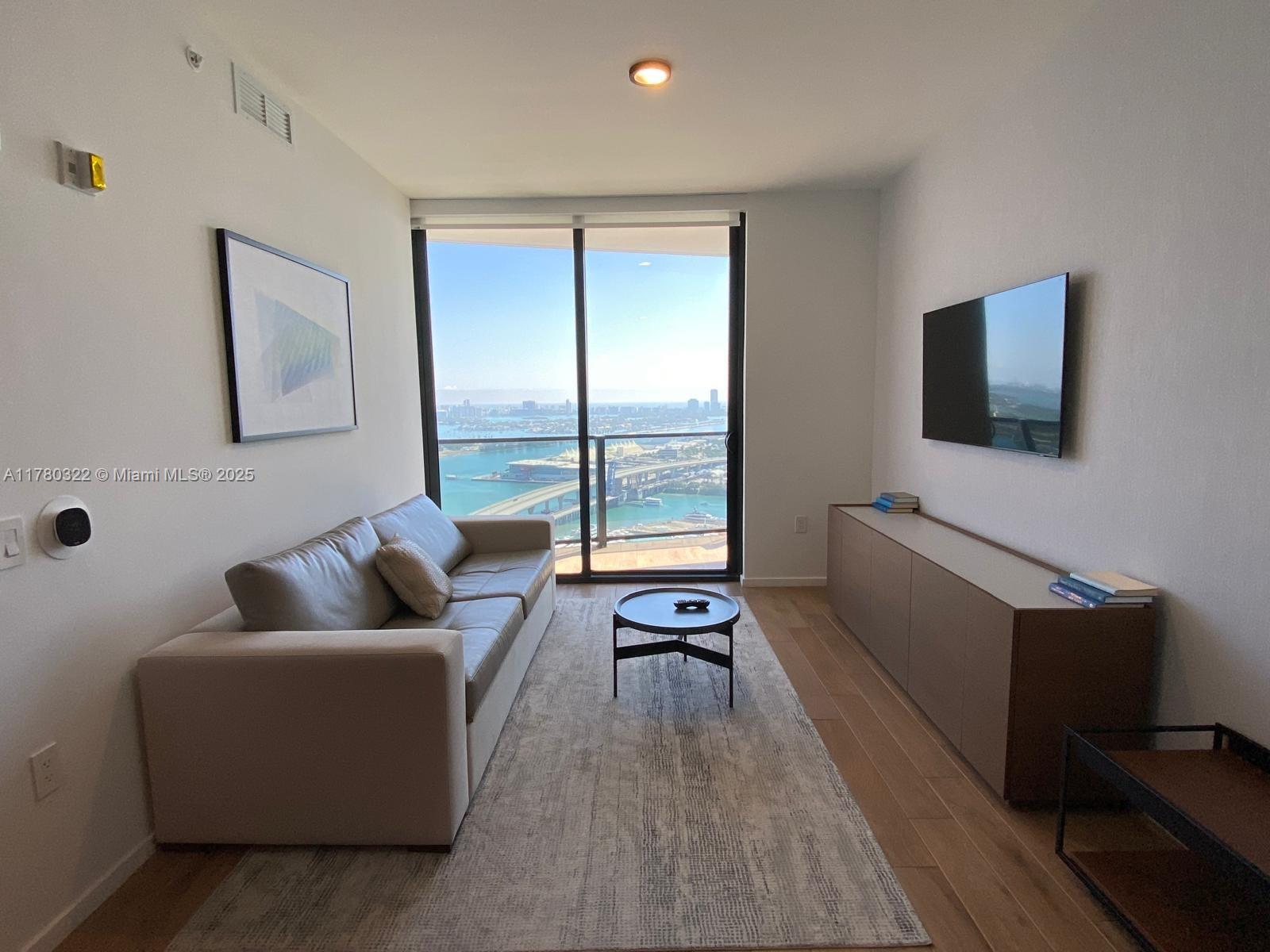 A living room features a sofa, coffee table, media console, and a balcony with water views — 398 NE 5th St # 2910, Miami FL 33132, MIAMI, FL
