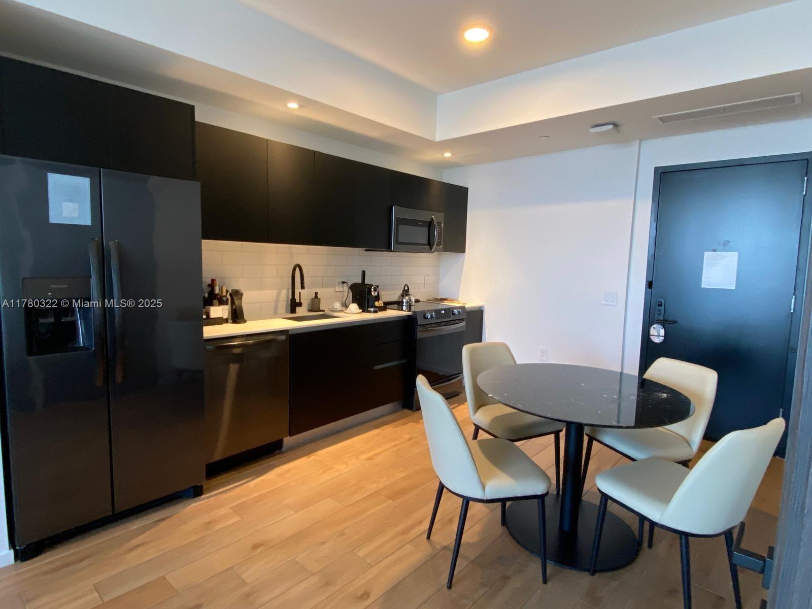 A modern kitchen features black cabinetry, stainless steel appliances, and a small round dining table — 398 NE 5th St # 2910, Miami FL 33132, MIAMI, FL