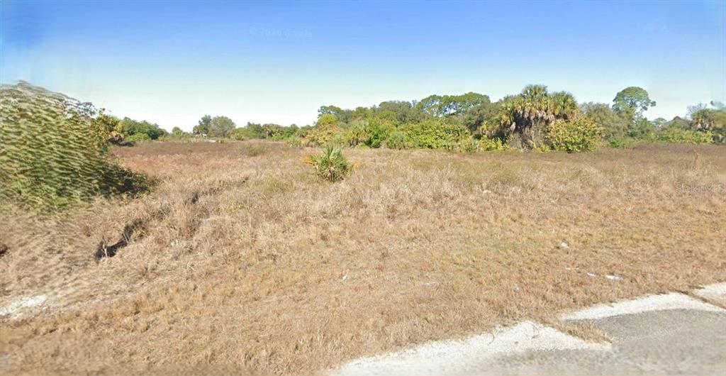 A vacant, grassy lot with scattered shrubs and trees under a clear blue sky — 769 SHARK LANE, LABELLE, FL